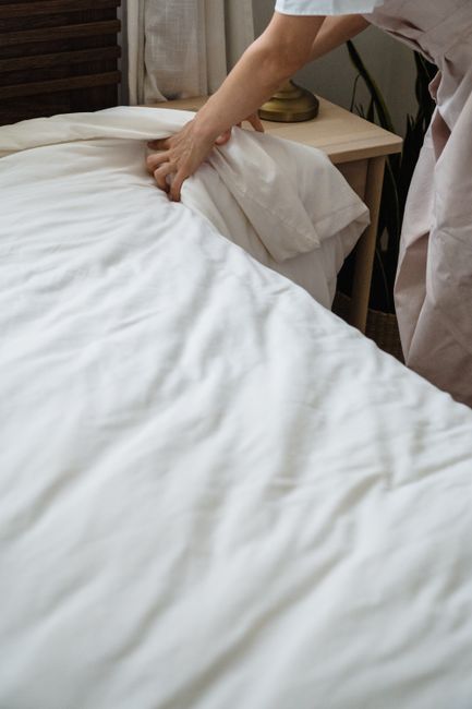 A modern bedroom with a neatly made bed featuring a bright turquoise upholstered headboard, situated against a beige patterned wallpaper. On each side of the bed are black bedside tables with matching